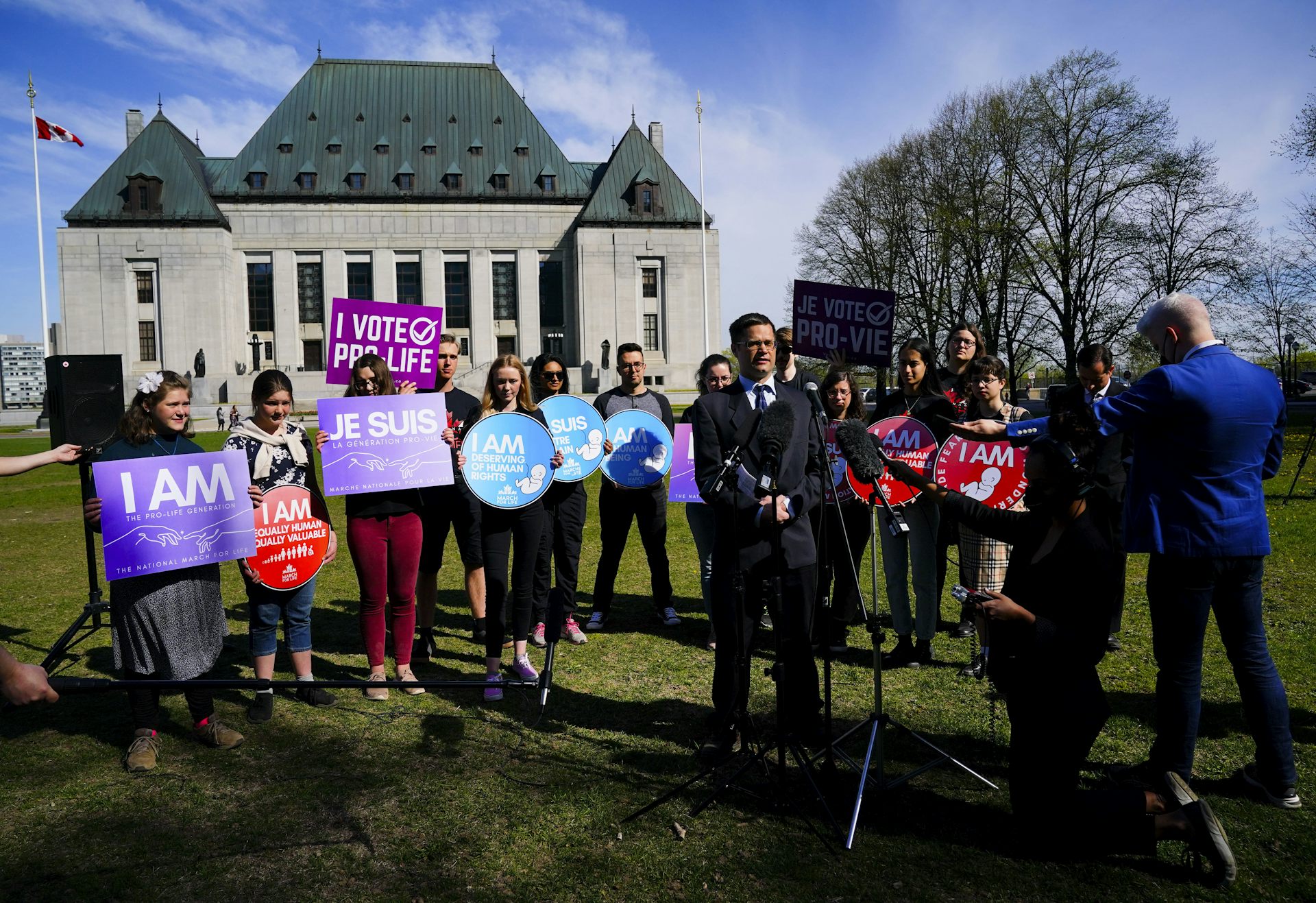 A group of people holding anti-abortion signs stand on the lawn of Canada's Supreme Court.