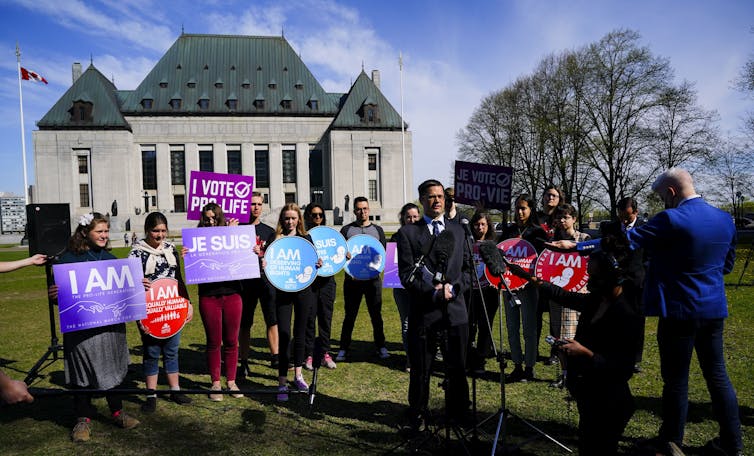 A group of people holding anti-abortion signs stand on the lawn of Canada's Supreme Court.