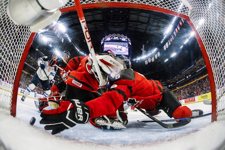 A camera shot from inside a hockey net as a goalie and player fill the space