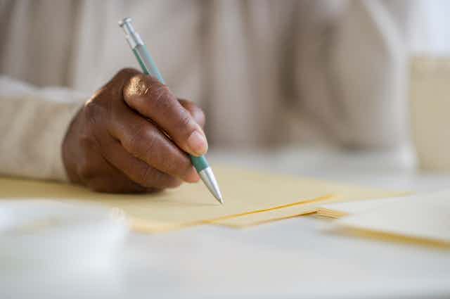 person sitting at a desk, holding a pen over a blank piece of stationary.