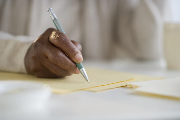 person sitting at a desk, holding a pen over a blank piece of stationary.
