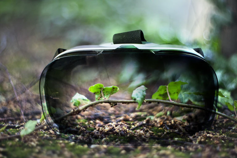 Virtual reality headset seen against a branch on a forest floor.