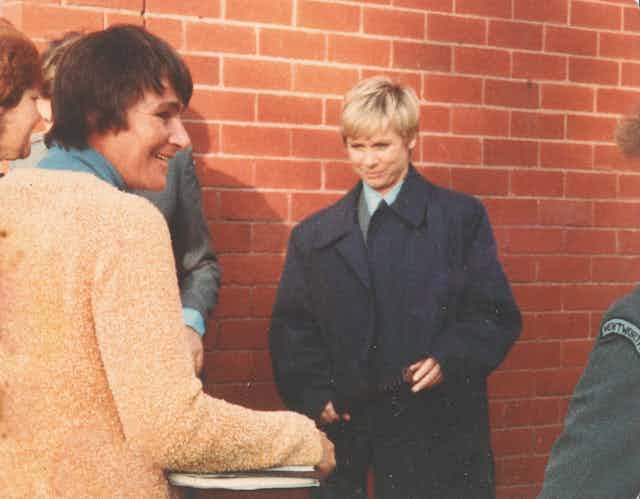 Woman smiling, turned away from a woman in a police uniform and coat