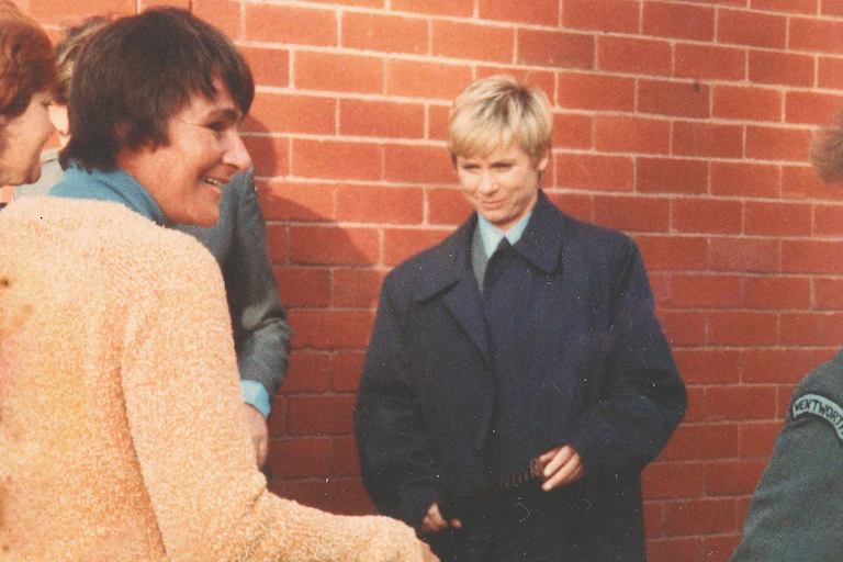 Woman smiling, turned away from a woman in a police uniform and coat