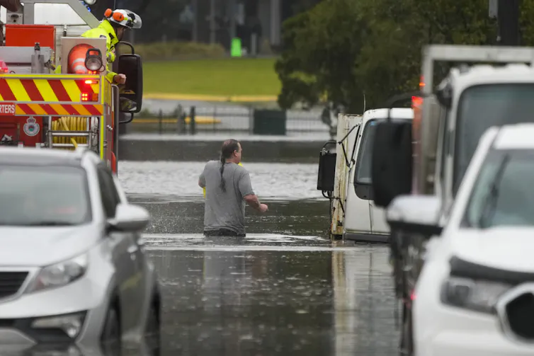 Man wades through floodwater beside a firetruck