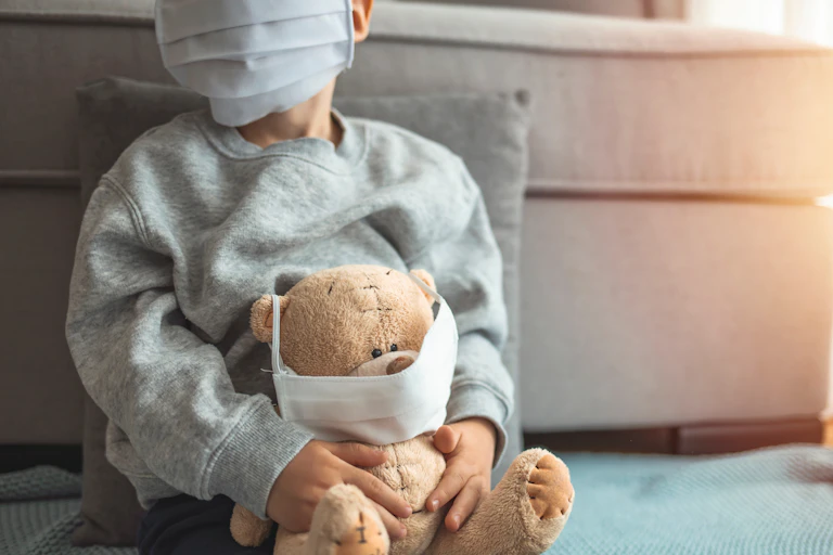 Child in a mask holds teddy, also in a mask