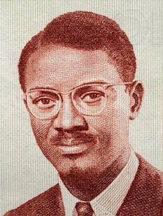 A portrait of a young man in glasses, suit and tie, wearing a moustache and goatee, his hair in a side path.