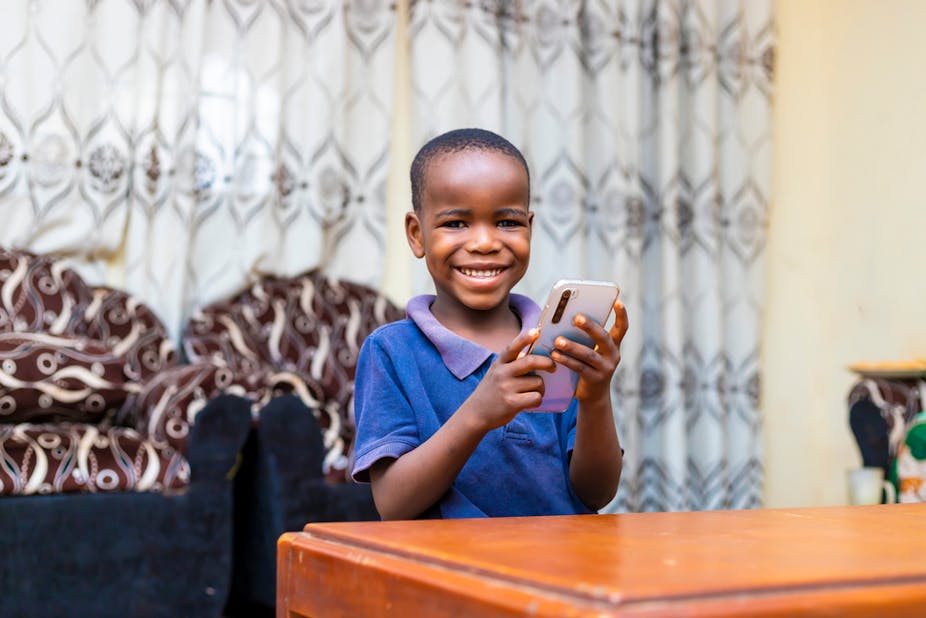 A young boy siting at a table at home using his mobile phone for online learning.