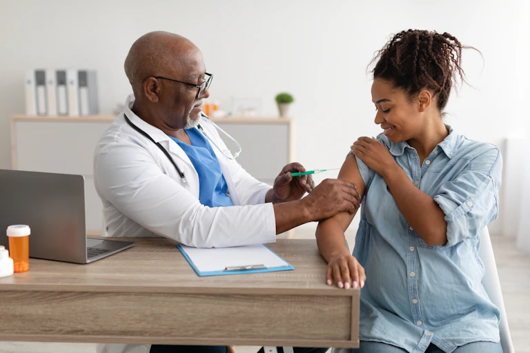 A doctor giving an injection to a pregnant woman on her upper arm.