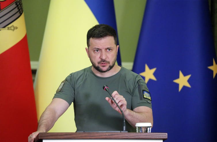 Ukrainian president, Volodymyr Zelensky, speaks in front of Ukrainian and EU flags.