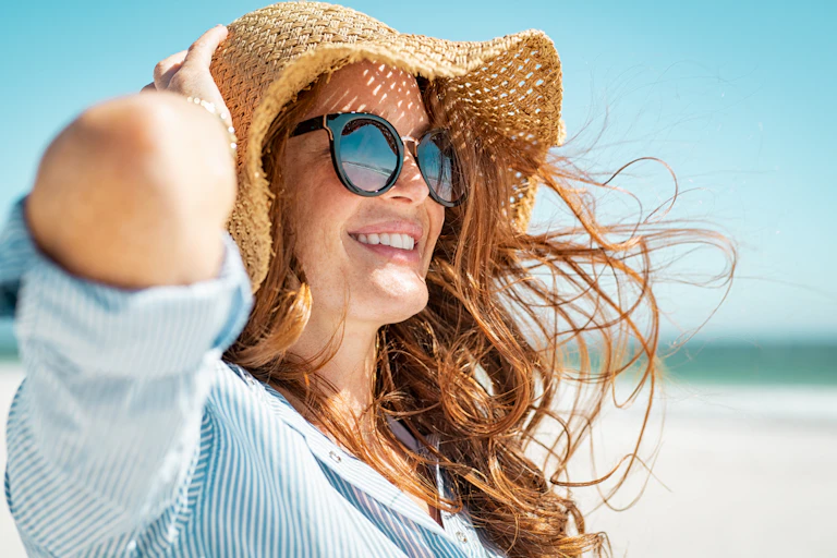 Une jeune femme se protège du soleil par des lunettes, un grand chapeau et une chemise ample