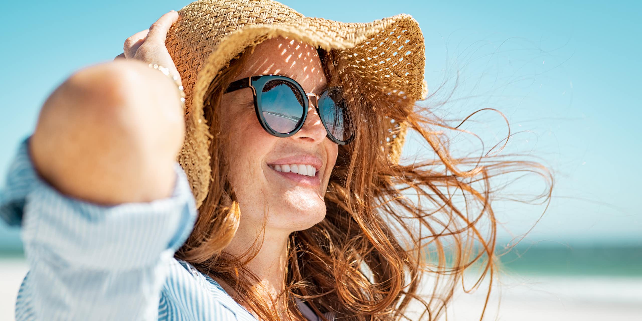 Une jeune femme se protège du soleil par des lunettes, un grand chapeau et une chemise ample
