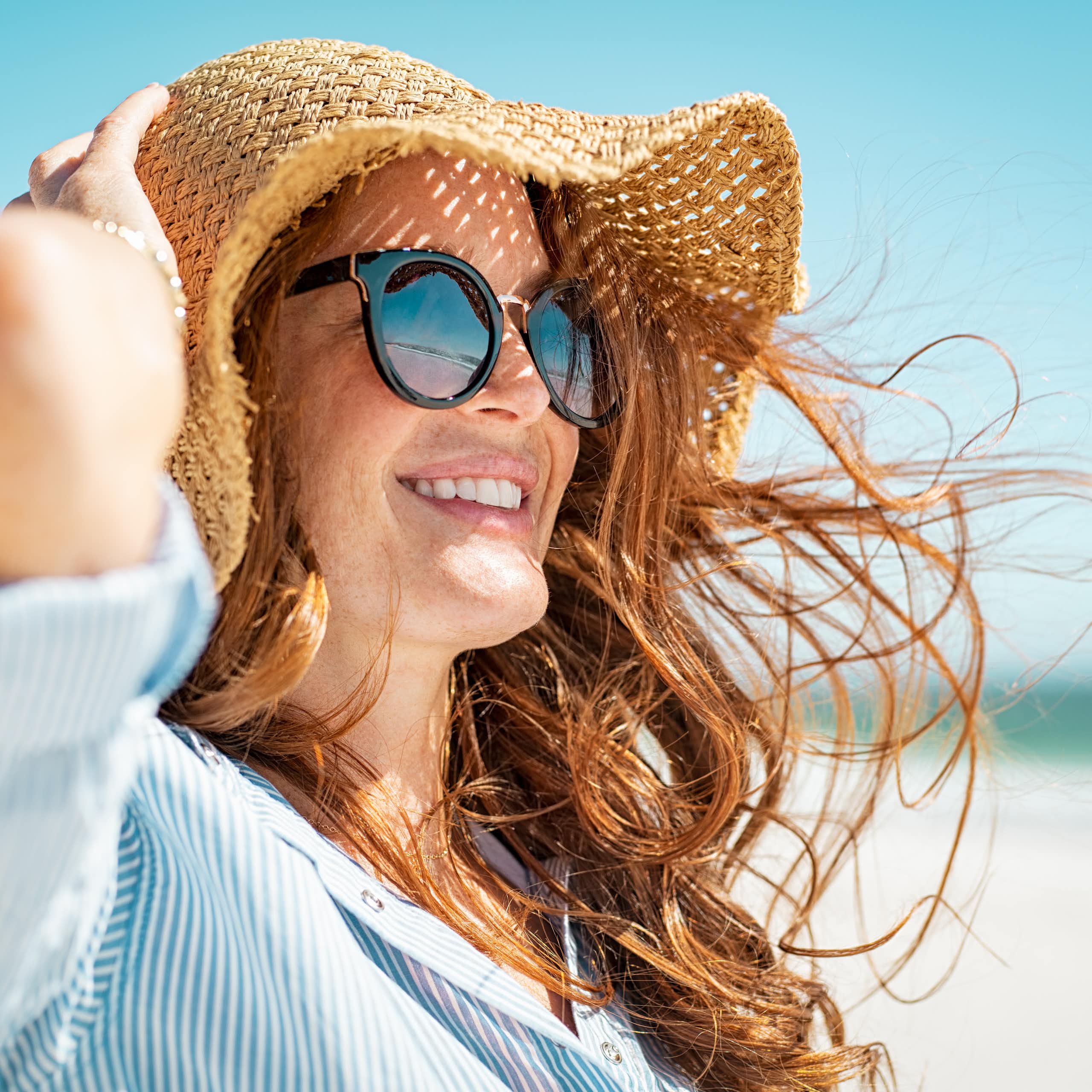 Une jeune femme se protège du soleil par des lunettes, un grand chapeau et une chemise ample
