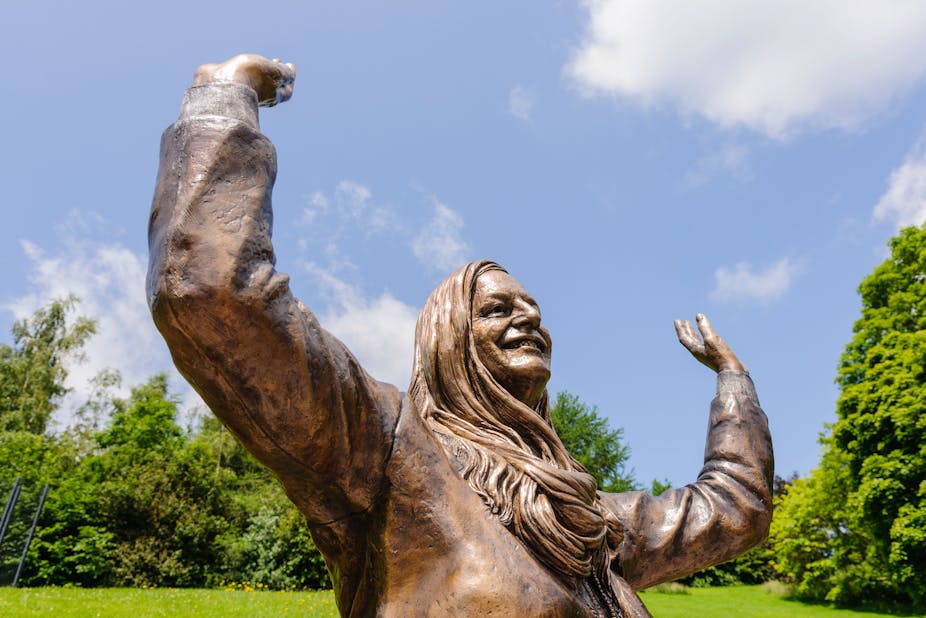 Bronze statue of Mary Peters, a woman with long hair, smiling with her hands in the air.