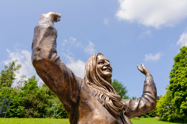 Bronze statue of Mary Peters, a woman with long hair, smiling with her hands in the air.