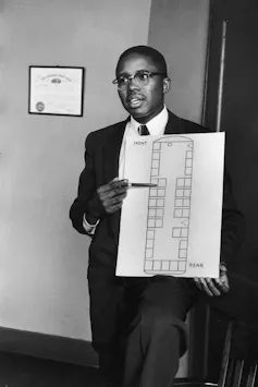 A man in a suit and tie, holding a seating diagram of a bus.