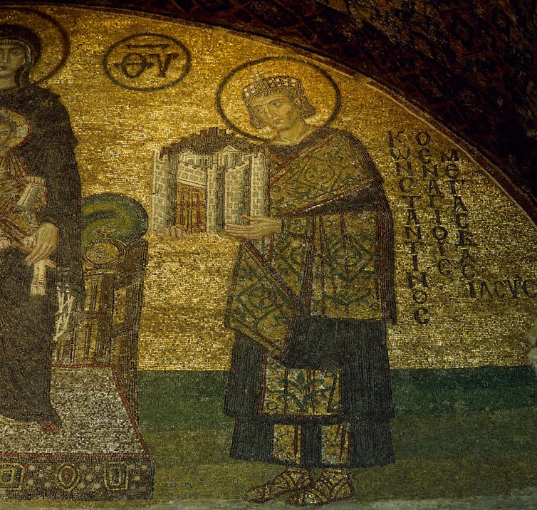 A golden mosaic shows a man with a halo holding a model city.