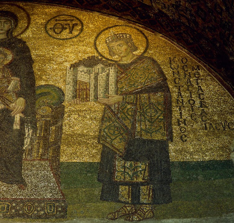 A gold mosaic shows a man with a halo holding up a model of a city.