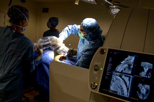Opération d'une tumeur avec le personnel médical autour du patient, et des IRM au premier plan