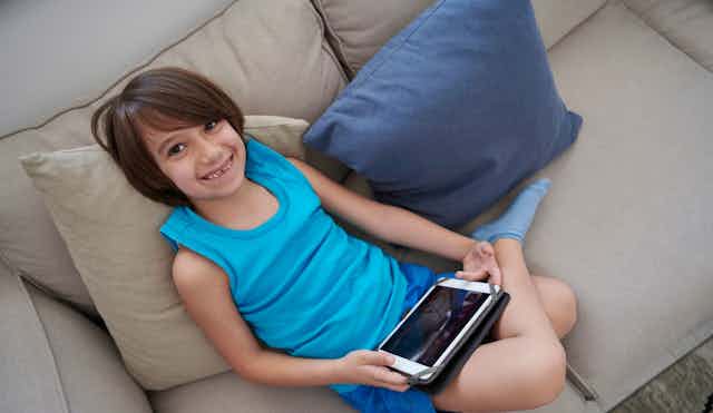 A child smiles holding a device on a laptop.