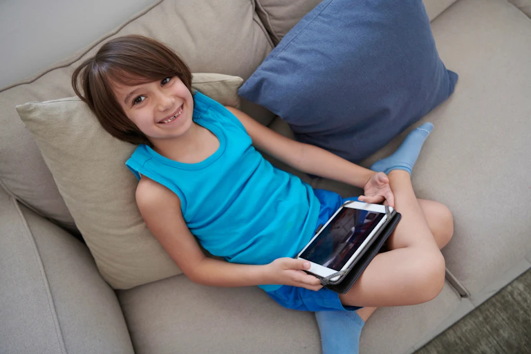 A child smiles holding a device on a laptop.