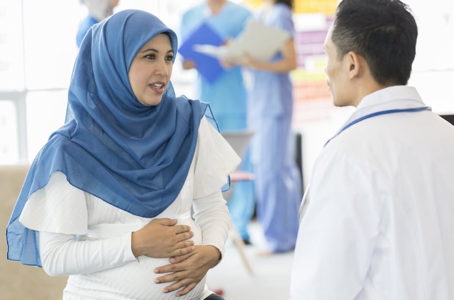 A woman wearing a blue headdress talking to a physician.