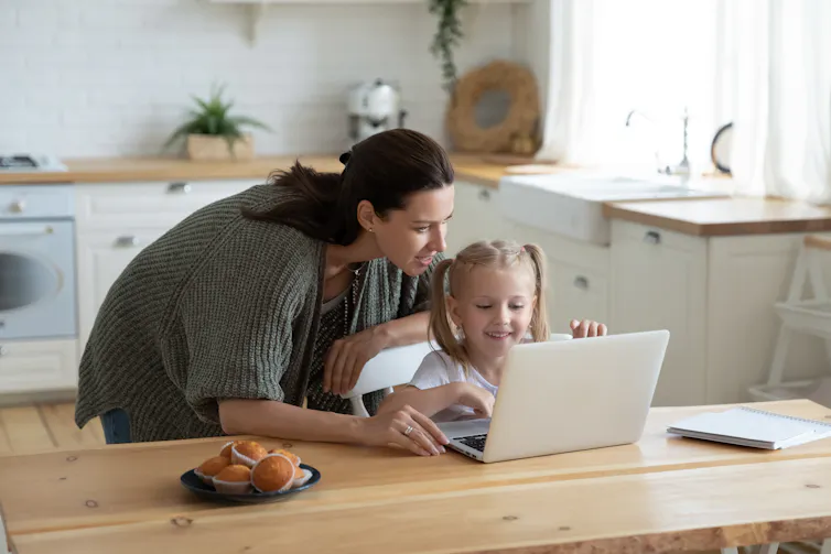 A mother seen at a laptop with a child.