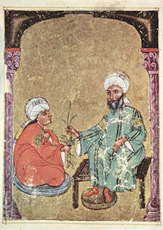 A 13th century folio showing a man with a beard and a turban giving herb to a person seated in front of him.