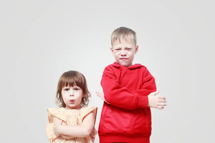 Siblings with arms crossed, pulling faces.