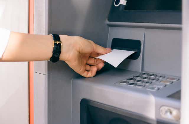 A hand pulls a blank slip of paper out of an ATM