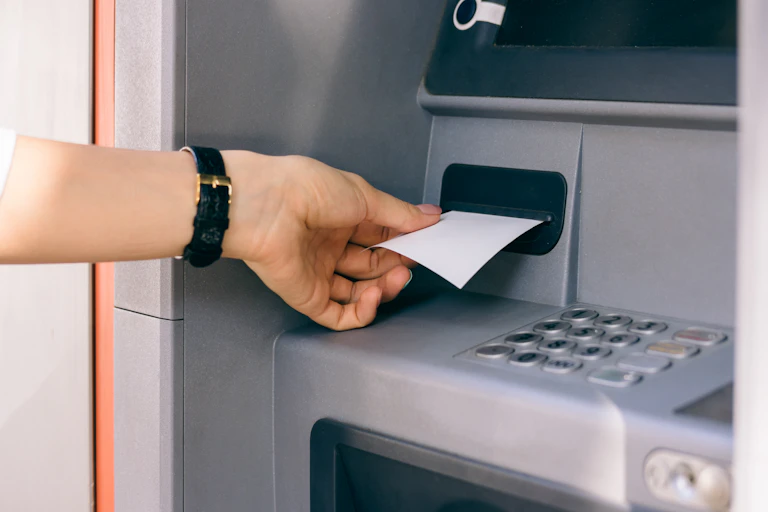 A hand pulls a blank slip of paper out of an ATM