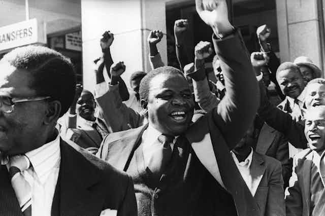 A group of men in suits, cheering and smiling, fists raised.