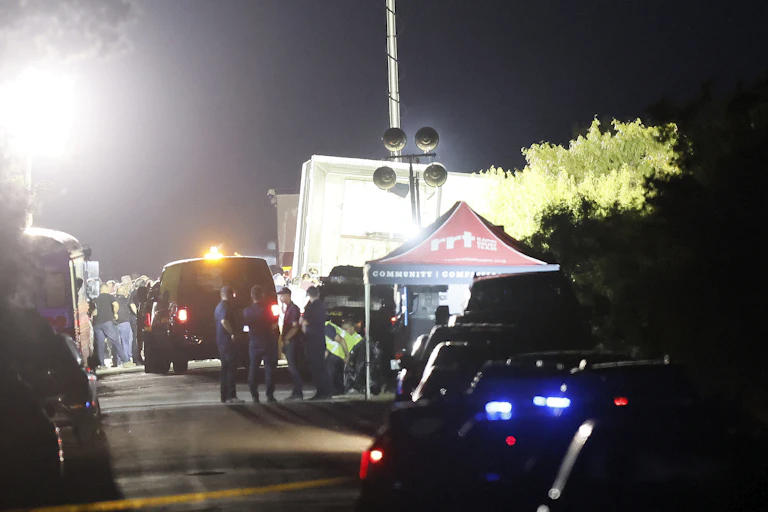 Police and officials man a roadblock near a tractor trailor on the side of the road leading to the location where more at least 46 migrants were reportedly found dead