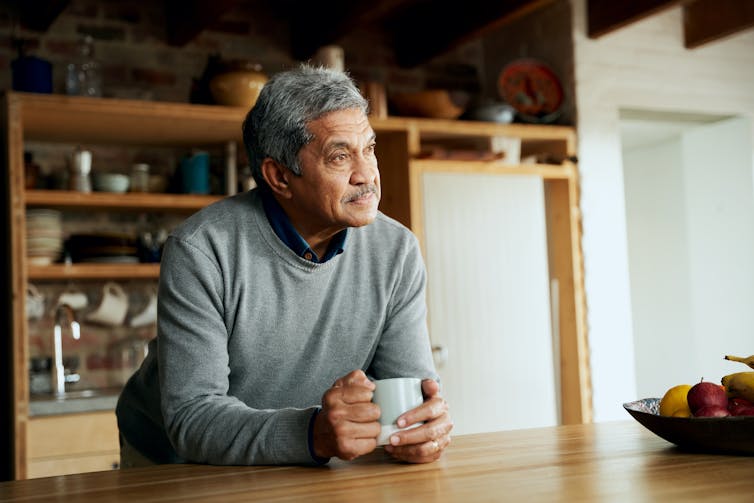 A man leans on the kitchen bench holding a mug.