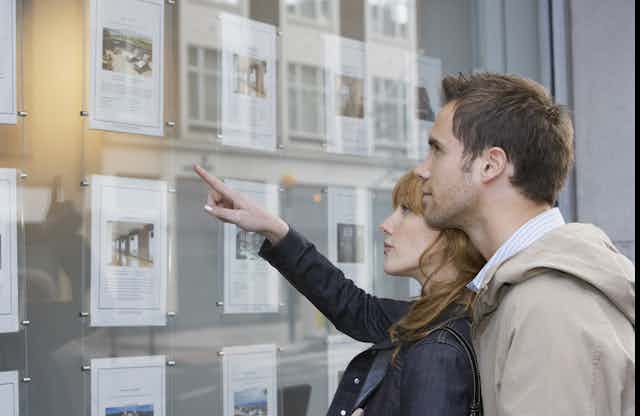 Two people look at house ads in an estate agent window