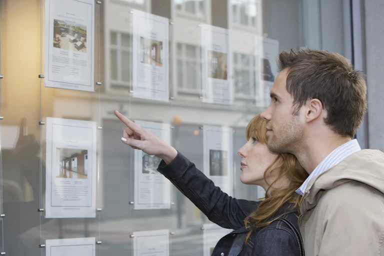 Two people look at house ads in an estate agent window