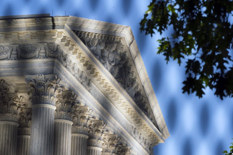 The ornate peak of a white stone building is seen through security fencing.