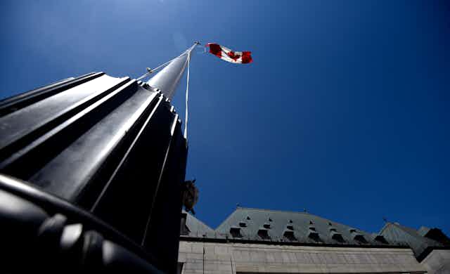 the canadian flag is seen flying from the foot of the flagpole over an ornate building