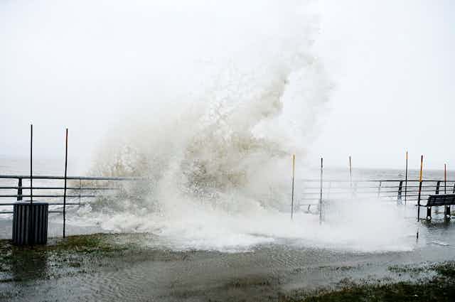 A large wave crashes over a boardwalk.