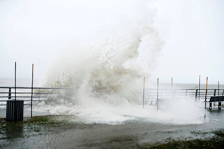 A large wave crashes over a boardwalk.