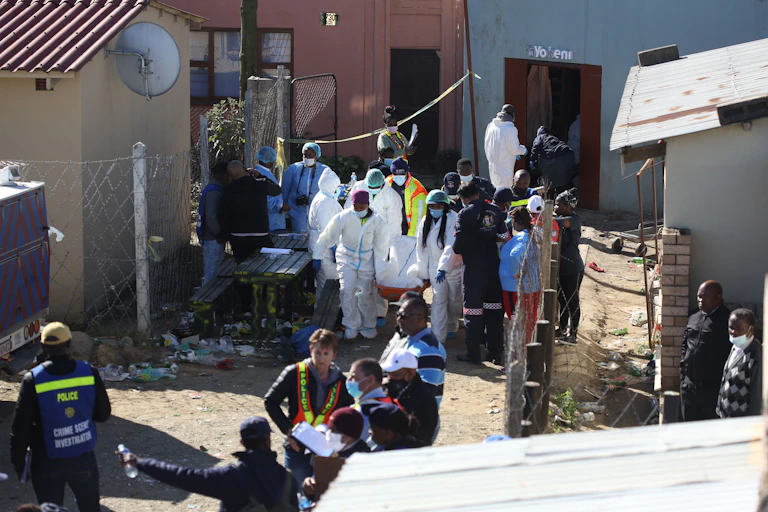 People weaing protective clothing carry a stretcher out of a building and people in police uniform stand nearby