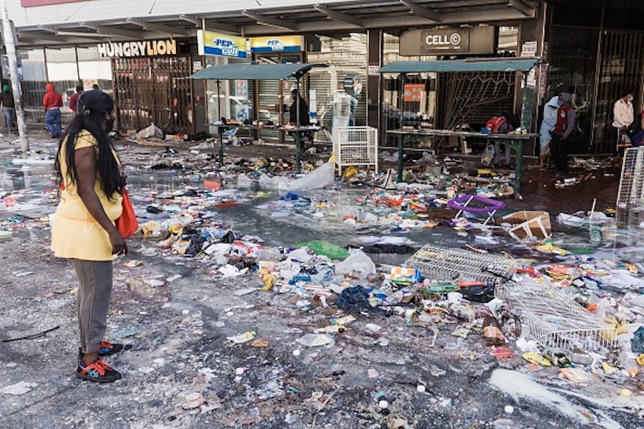 A woman stands on a street strewn with debris from the looting and destruction of shops.