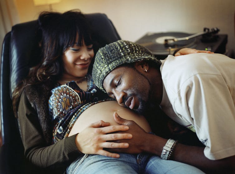 man listens lovingly to smiling woman's pregnant belly
