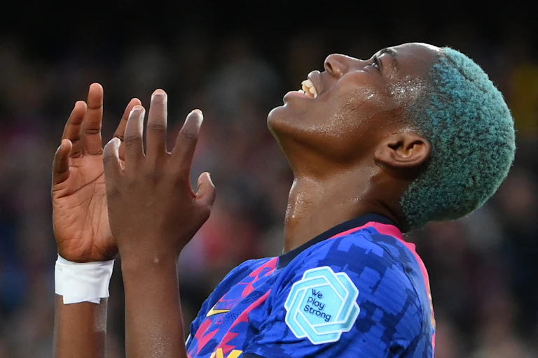 A woman with green dyed hair looks heavenward, her hands up in despair. She wears a football jersey.