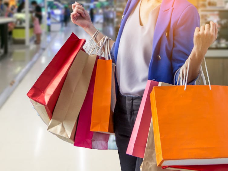 Neck-down photo of woman with lots of colourful shopping bags on her arms.