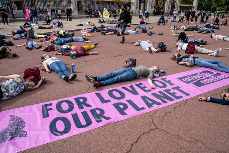 People lie separately on the ground alongside a sign reading 'For Love Of Our Planet'