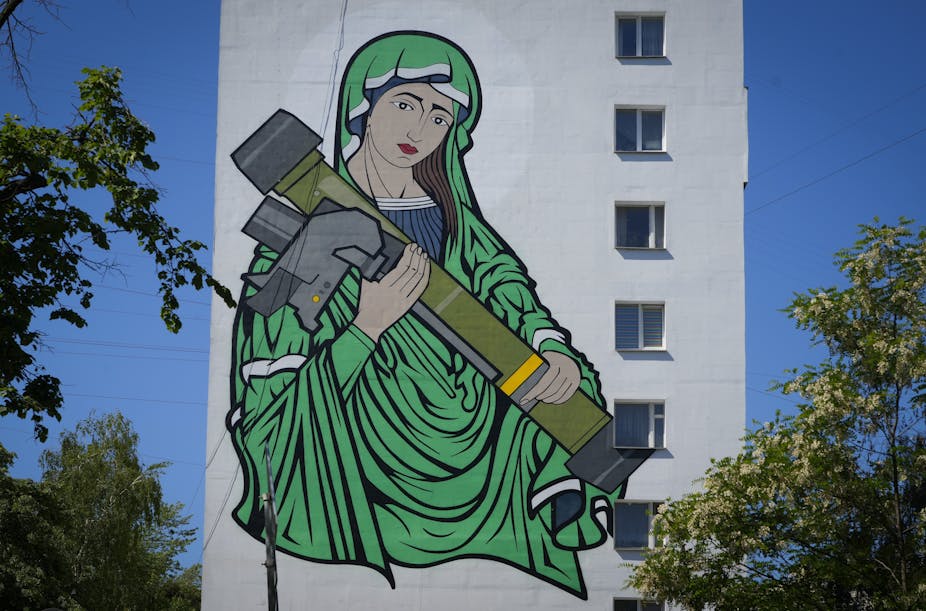 A mural on the side of an apartment building shows a woman in a green cloak holding a weapon.
