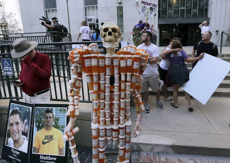 Protesters with signs and a skeleton made of pill bottles outside a building
