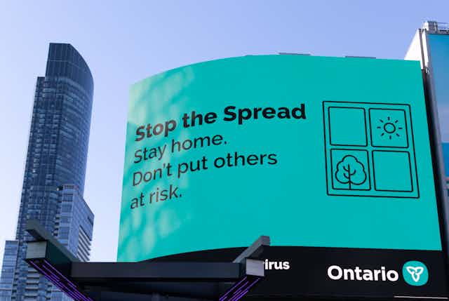 a sign with black text on a light teal background reading STOP THE SPREAD. STAY HOME. DON'T PUT OTHERS AT RISK.
