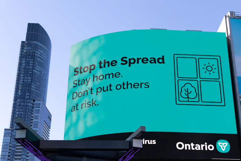a sign with black text on a light teal background reading STOP THE SPREAD. STAY HOME. DON'T PUT OTHERS AT RISK.
